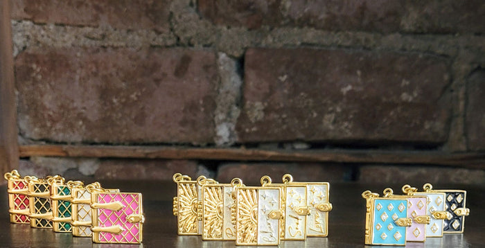 On the left hand side, all the Secret Diary Book Locket charms are lined up, in the middle all of the Secret Scripture Locket charms are lined up, and on the right all of the Stardust Book Locket charms lined up in front of a brick wall